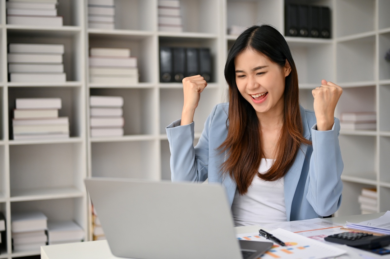 Smiling women at computer with hands up in the air